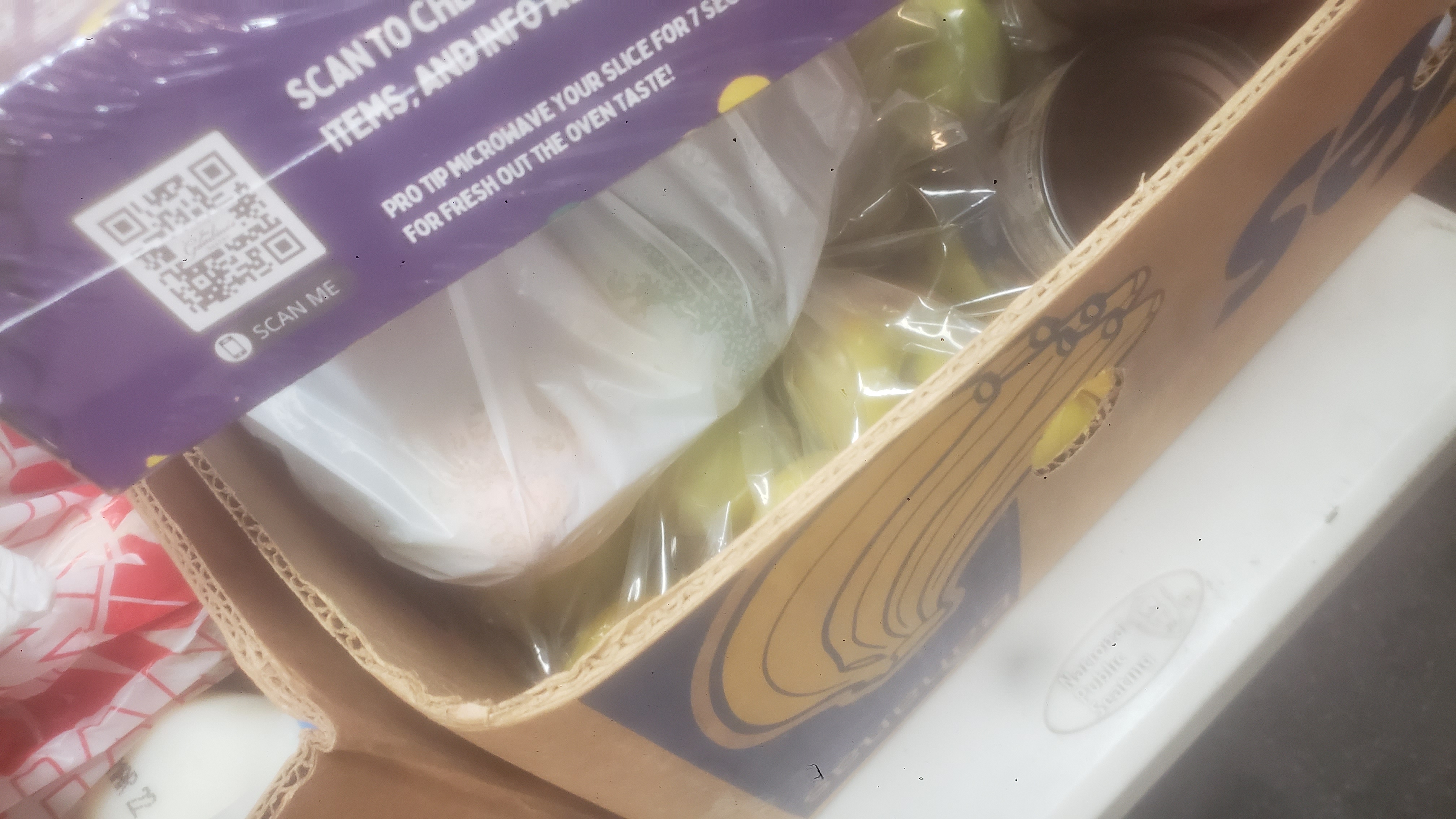 Banana box full of different foods with a sheet of king cake on top.
